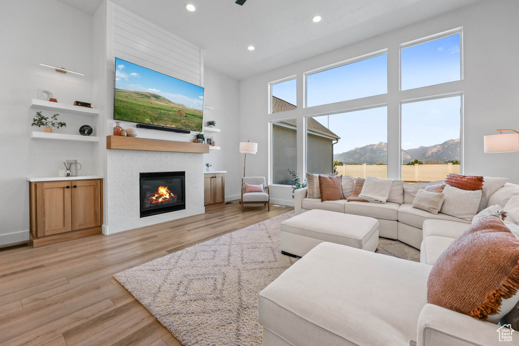 Living room featuring a glass covered fireplace, recessed lighting, light wood-style flooring, and a high ceiling