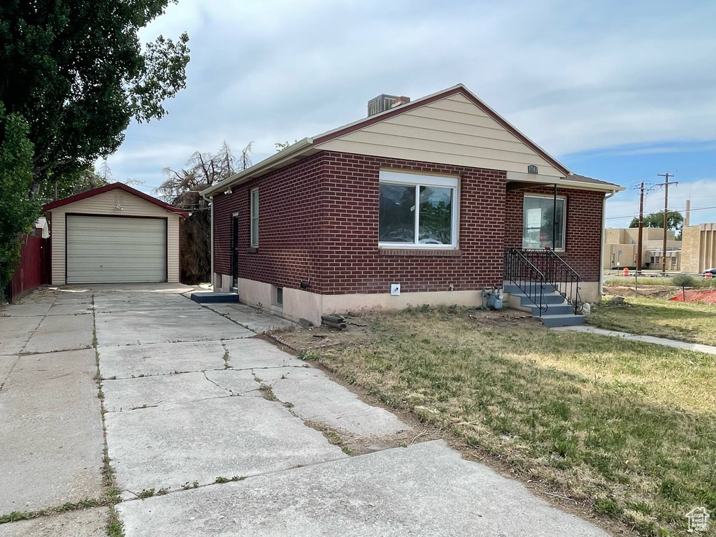 View of front of property featuring an outbuilding, brick siding, a front lawn, and driveway