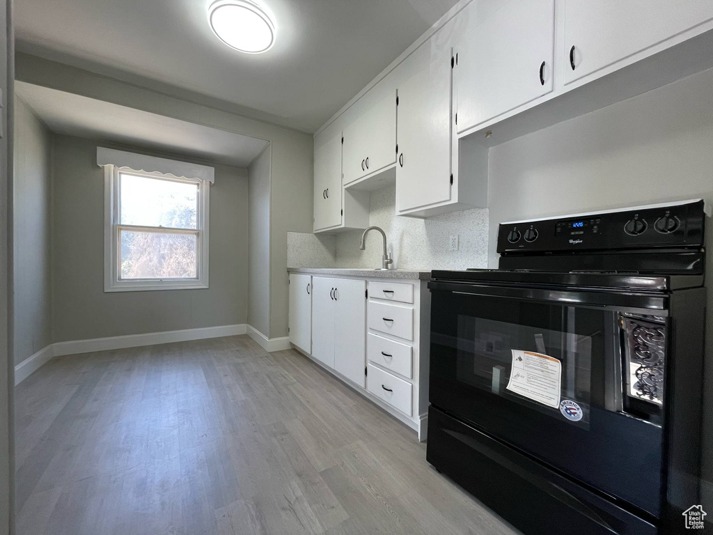 Kitchen with electric range, light wood-style flooring, and white cabinetry