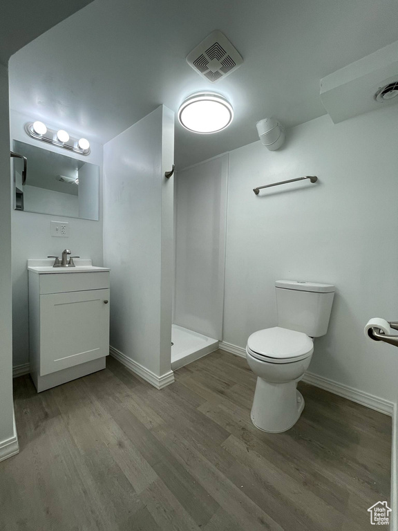 Bathroom with wood finished floors, a stall shower, toilet, vanity, and baseboards