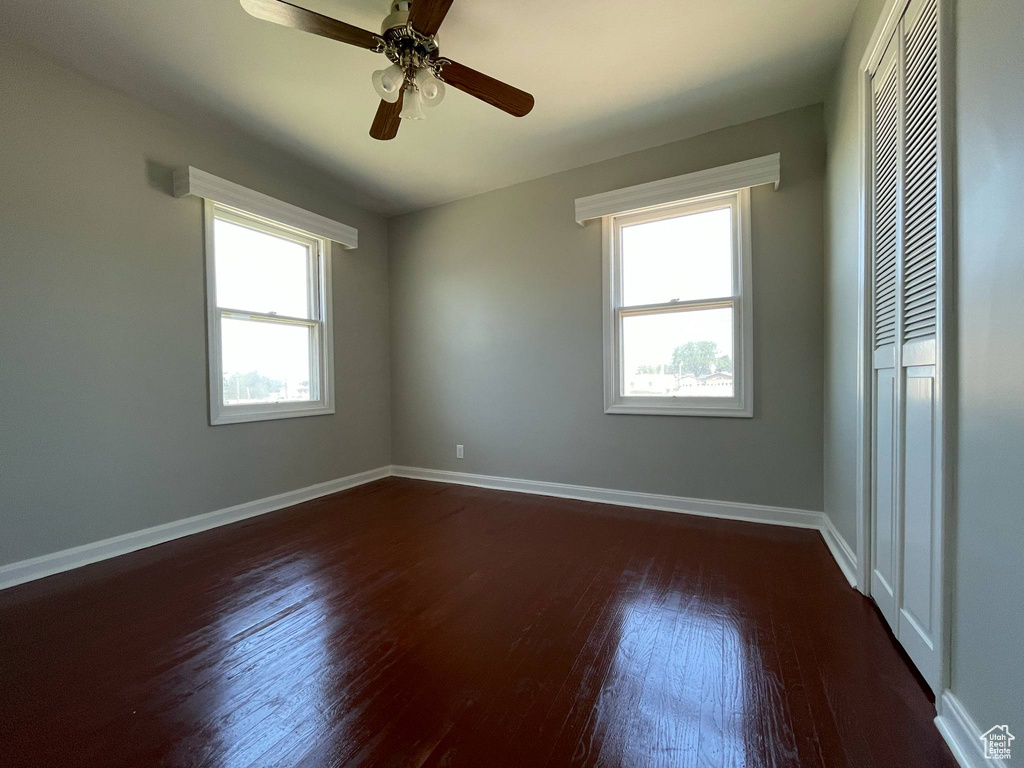 Empty room with dark wood-style flooring, plenty of natural light, baseboards, and ceiling fan
