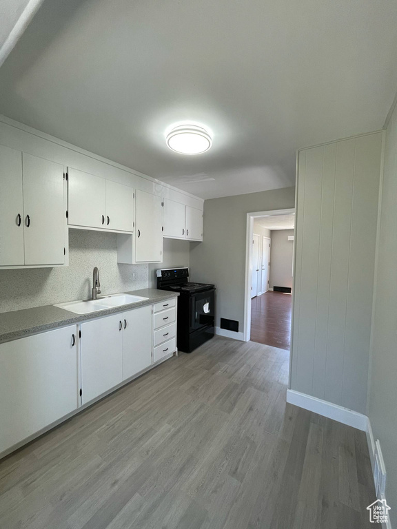 Kitchen with black / electric stove, a sink, light wood-style floors, white cabinetry, and light countertops