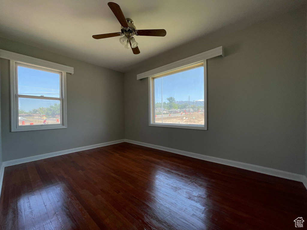 Empty room with dark wood-style flooring, baseboards, and a ceiling fan