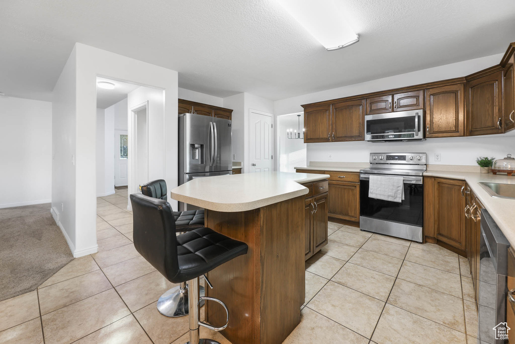 Kitchen with appliances with stainless steel finishes, a center island, light countertops, light tile patterned floors, and a breakfast bar