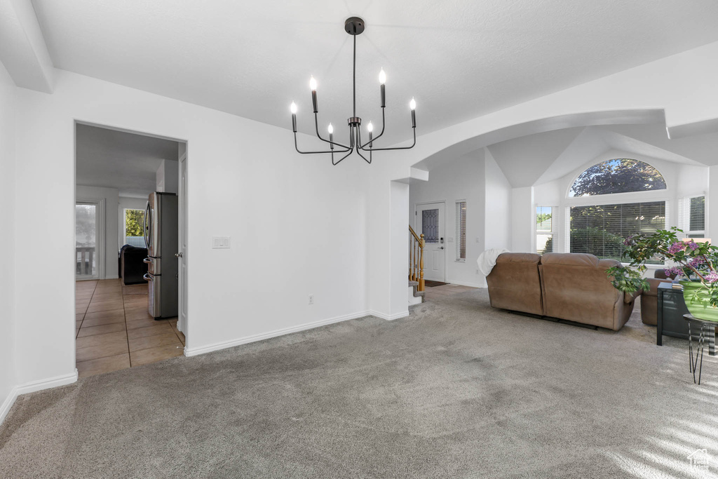 Carpeted dining area with arched walkways, plenty of natural light, a chandelier, vaulted ceiling, and stairway