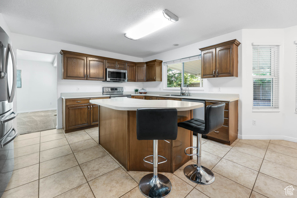 Kitchen featuring appliances with stainless steel finishes, light countertops, a kitchen island, a breakfast bar, and light tile patterned flooring
