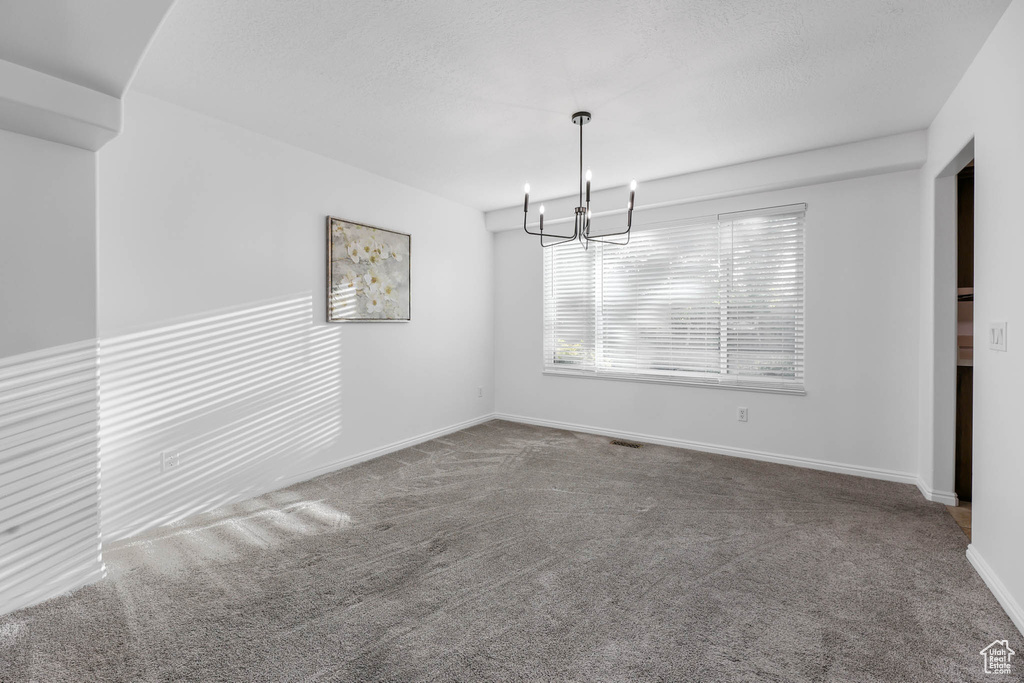 Carpeted empty room featuring a chandelier and baseboards