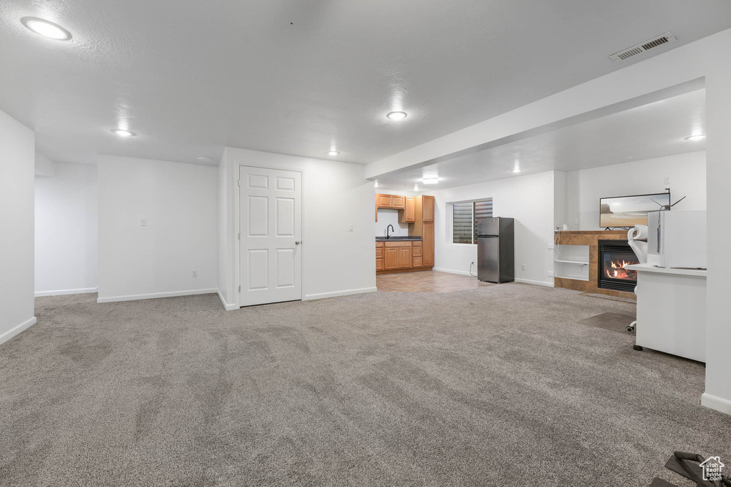 Unfurnished living room featuring a tiled fireplace, light colored carpet, and recessed lighting