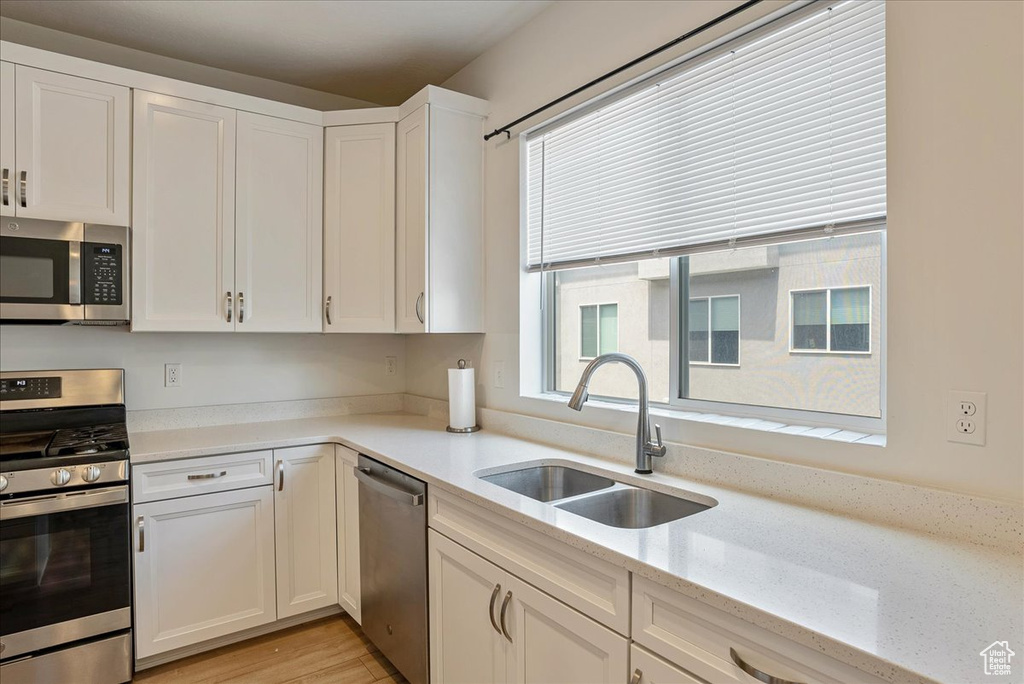 Kitchen featuring stainless steel appliances, white cabinetry, light stone countertops, and light wood finished floors