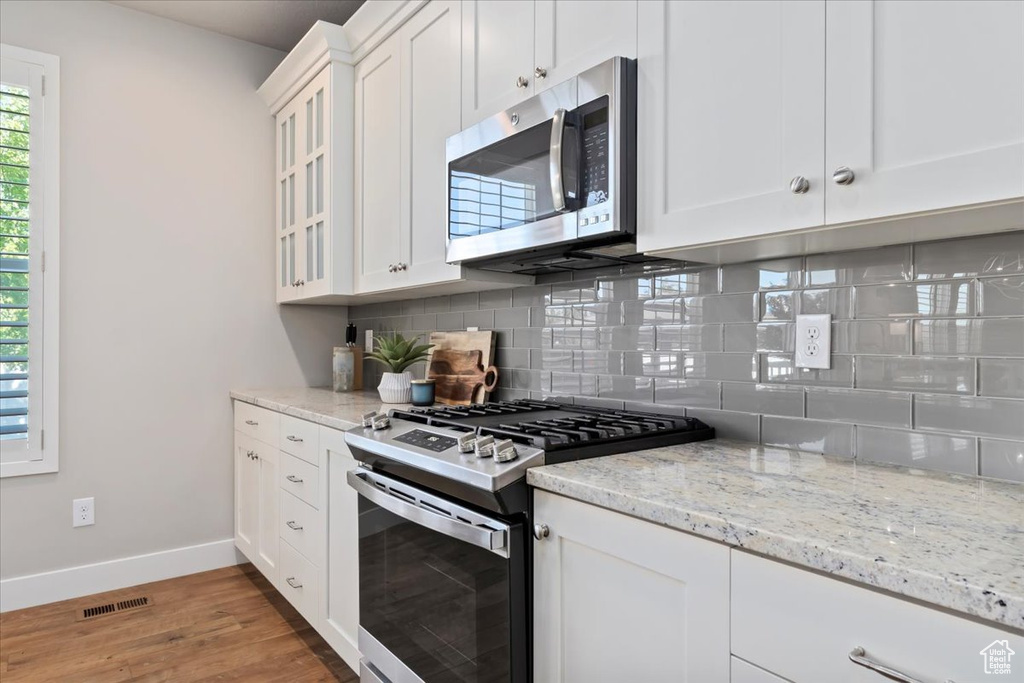 Kitchen featuring appliances with stainless steel finishes, light wood-style floors, decorative backsplash, white cabinetry, and light stone counters