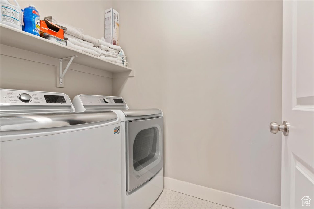Washroom with washing machine and dryer and light tile patterned flooring
