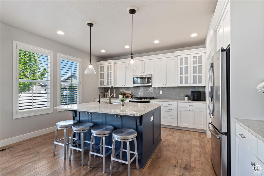 Kitchen featuring appliances with stainless steel finishes, hardwood / wood-style flooring, backsplash, white cabinets, and recessed lighting