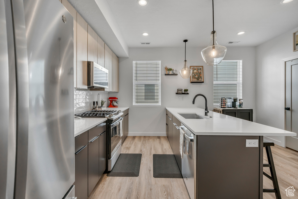 Kitchen featuring appliances with stainless steel finishes, a peninsula, a kitchen bar, light countertops, and light wood-type flooring