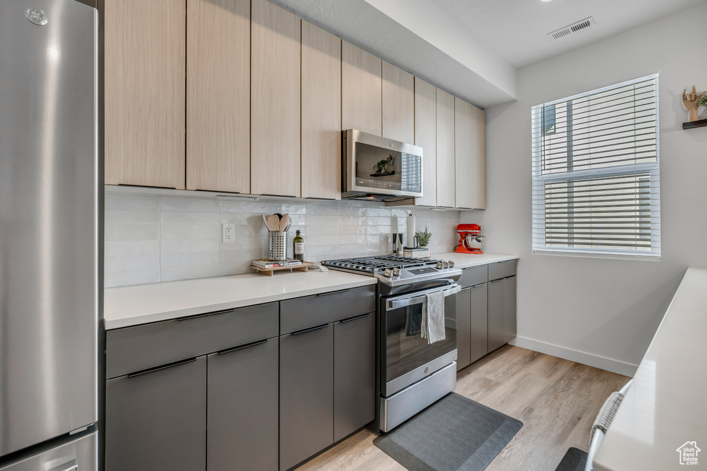 Kitchen featuring stainless steel appliances, gray cabinets, tasteful backsplash, light countertops, and light wood-type flooring