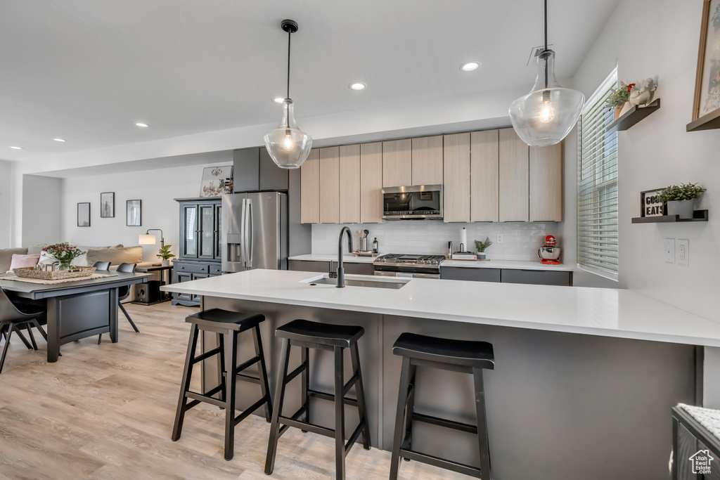 Kitchen with stainless steel appliances, light countertops, backsplash, modern cabinets, and a kitchen bar