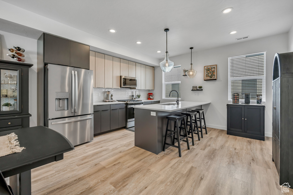 Kitchen with stainless steel appliances, a breakfast bar area, light countertops, recessed lighting, and light wood-type flooring