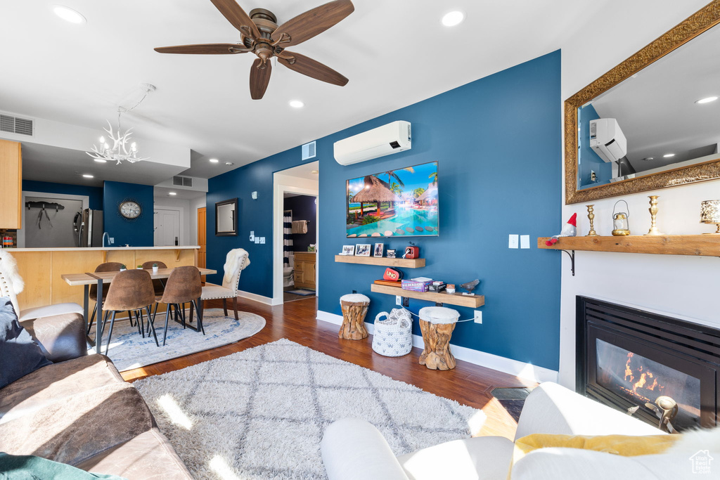 Living room featuring an AC wall unit, wood finished floors, a chandelier, baseboards, and ceiling fan