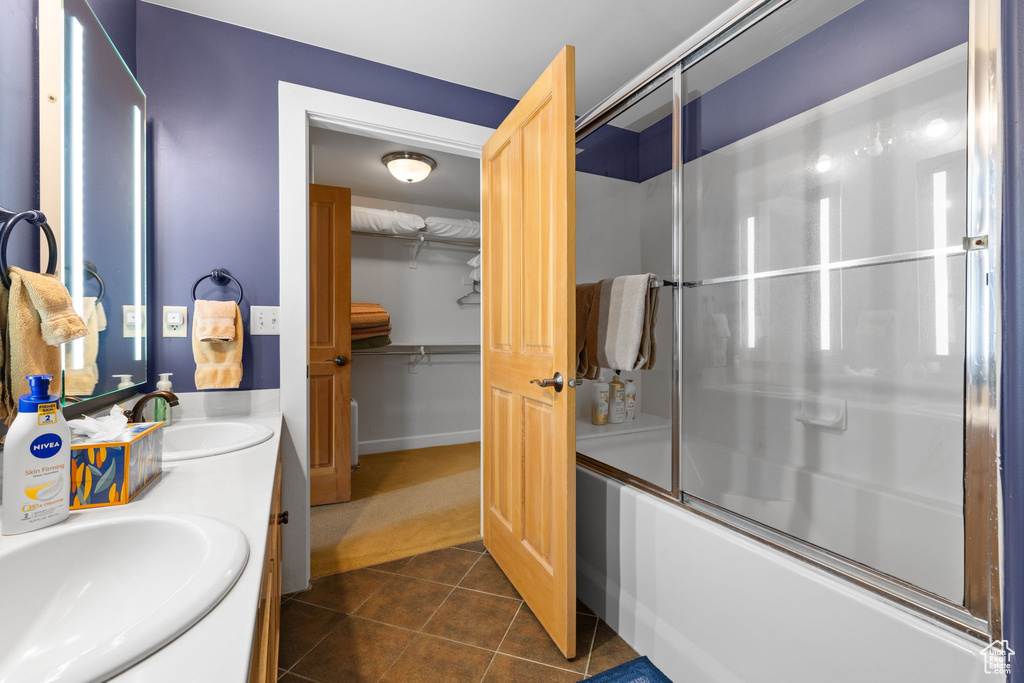 Bathroom featuring bath / shower combo with glass door, double vanity, tile patterned flooring, baseboards, and a walk in closet