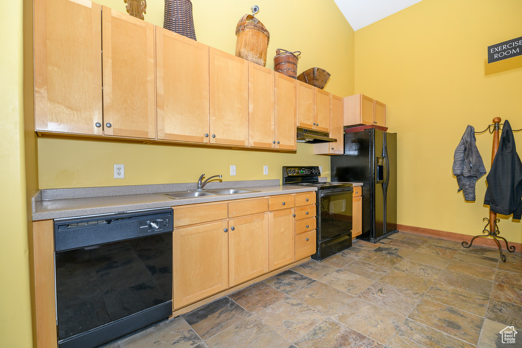 Kitchen featuring black appliances, a sink, under cabinet range hood, light stone finish flooring, and light brown cabinetry