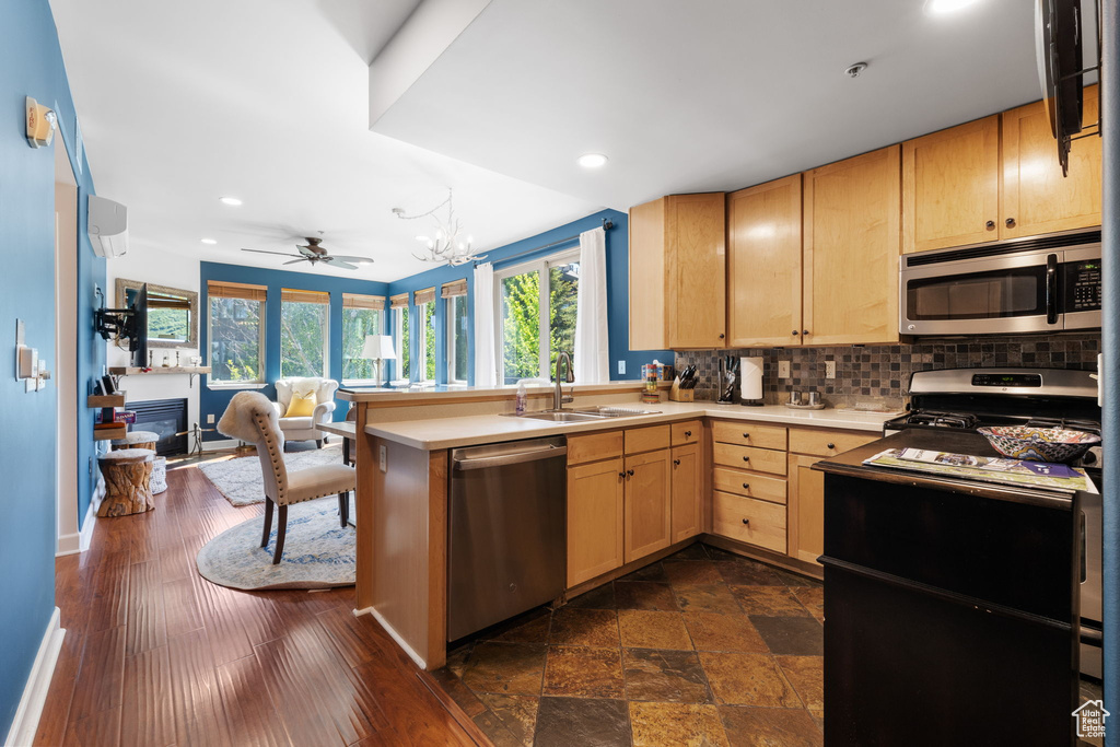 Kitchen featuring appliances with stainless steel finishes, a sink, light brown cabinetry, decorative backsplash, and a peninsula