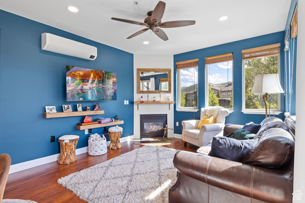 Living room featuring a wall unit AC, a glass covered fireplace, recessed lighting, wood finished floors, and a ceiling fan