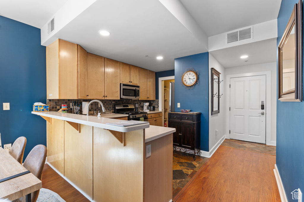 Kitchen with appliances with stainless steel finishes, baseboards, a breakfast bar area, tasteful backsplash, and a peninsula