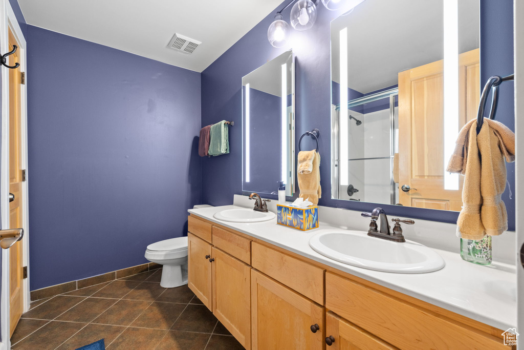 Full bath with toilet, double vanity, an enclosed shower, and tile patterned flooring