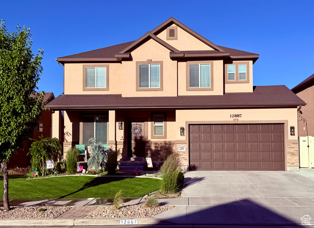 View of front facade with stucco siding, concrete driveway, a front yard, and an attached garage
