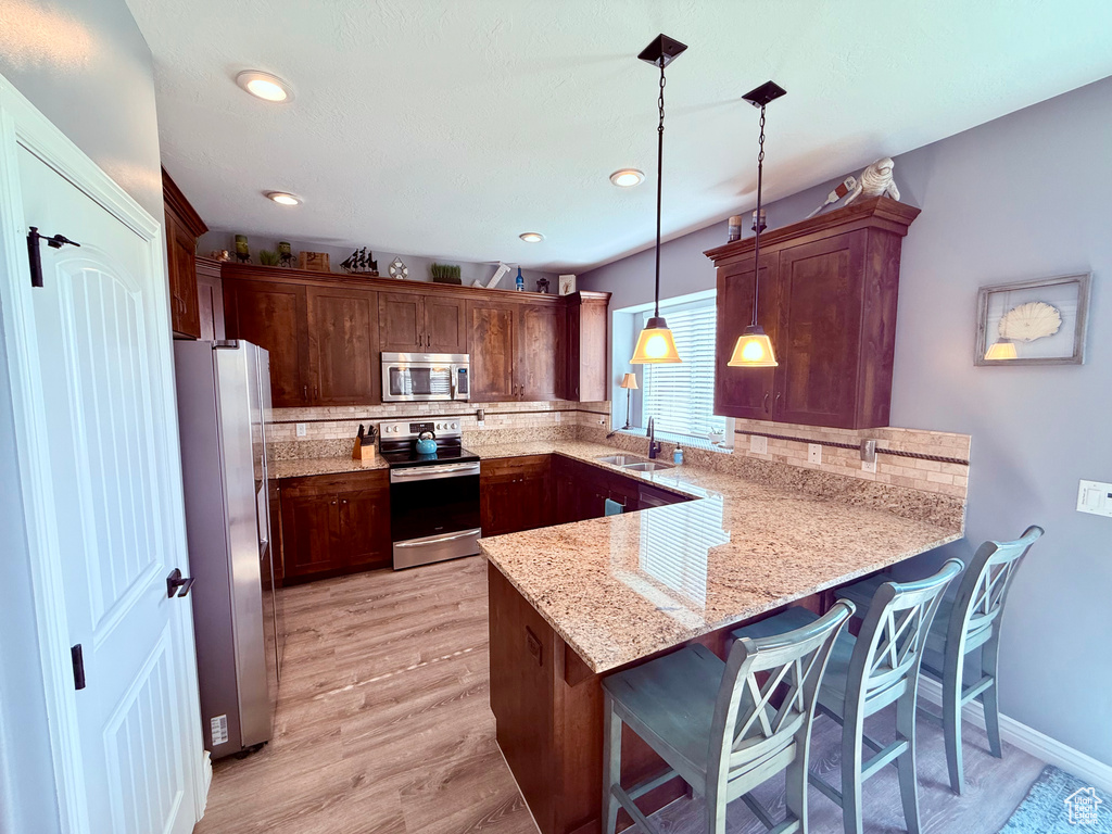 Kitchen with appliances with stainless steel finishes, a peninsula, backsplash, light wood-style flooring, and light stone counters