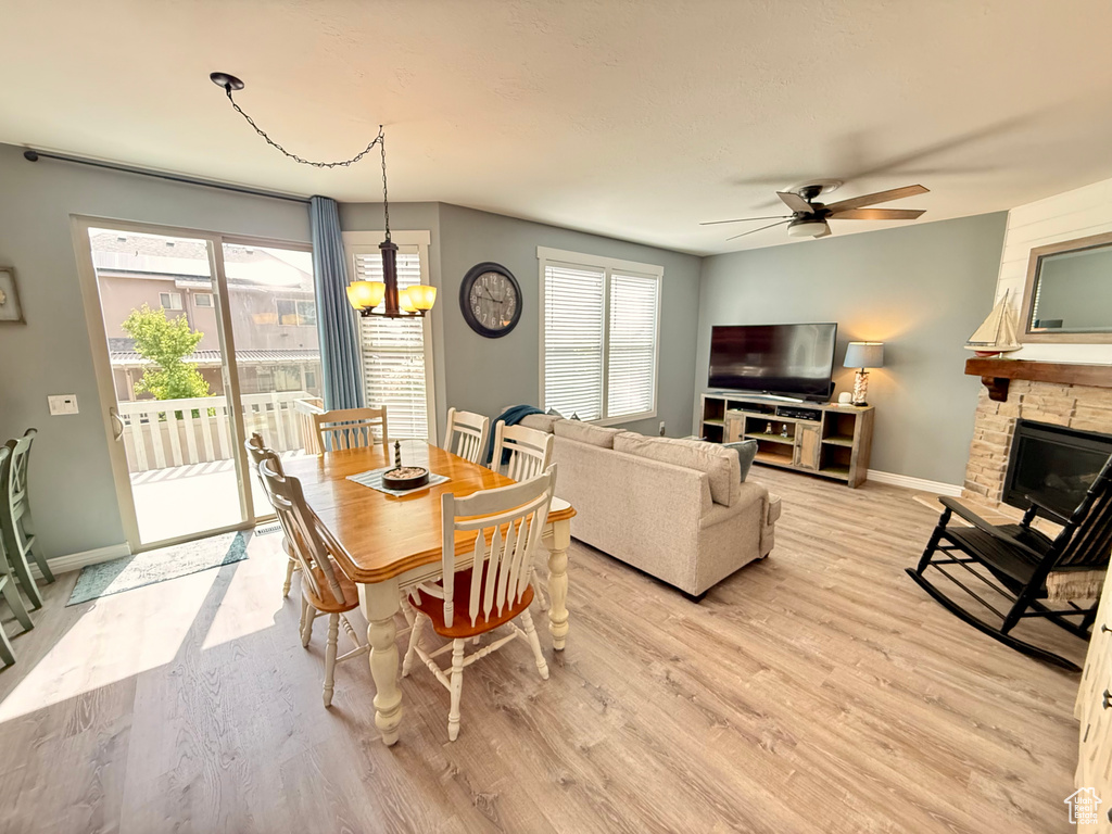 Dining room with a ceiling fan, light wood-type flooring, a chandelier, a fireplace, and plenty of natural light
