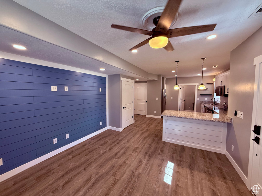 Kitchen with white cabinets, a ceiling fan, light stone counters, a peninsula, and dark wood-style floors