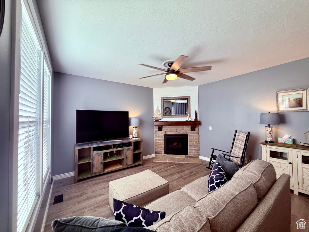 Living area featuring ceiling fan, a fireplace, wood finished floors, and a textured ceiling