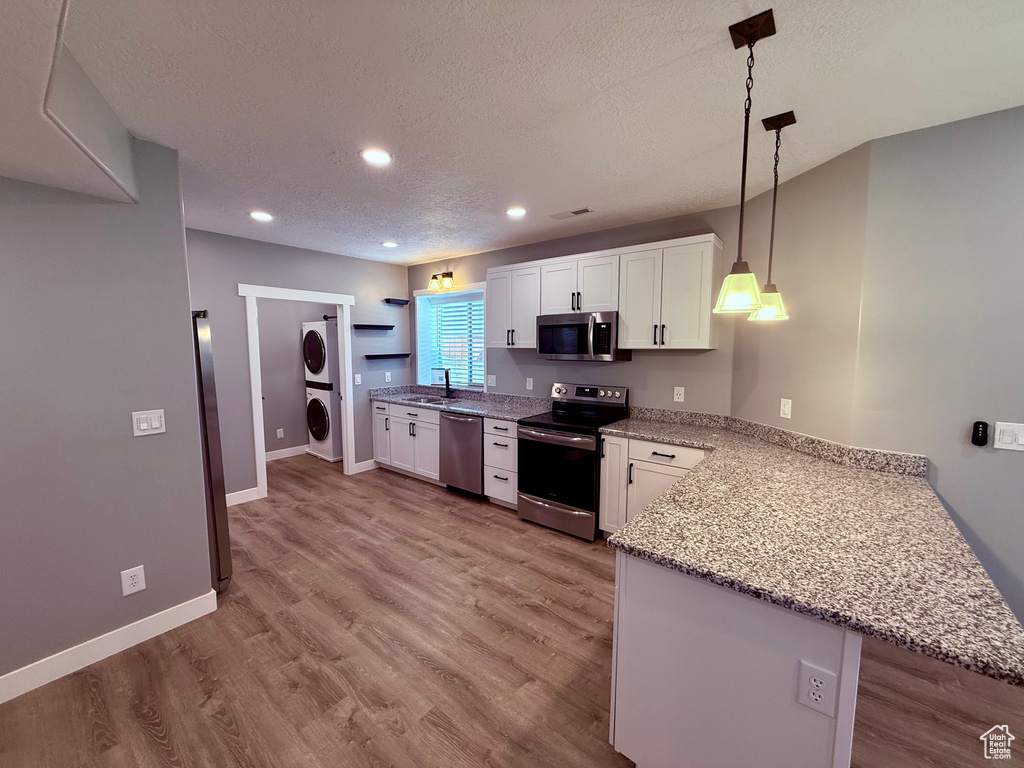 Kitchen featuring stainless steel appliances, stacked washer and clothes dryer, white cabinets, a peninsula, and a textured ceiling