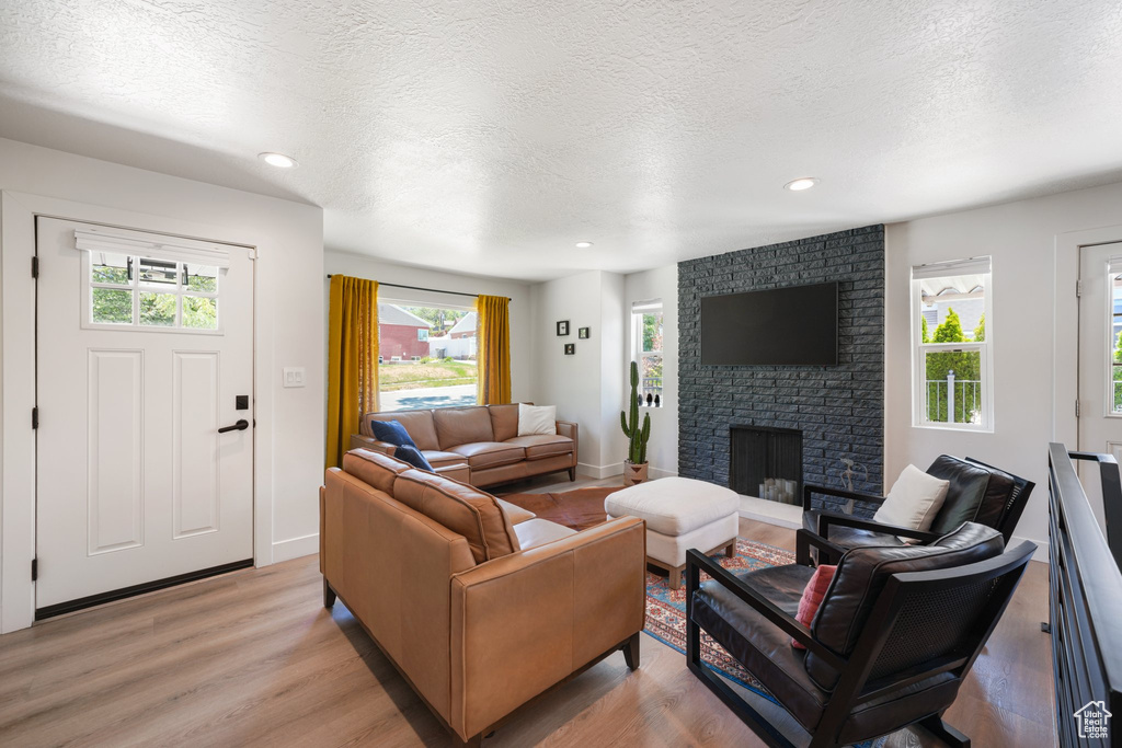 Living room with light wood finished floors, a fireplace, a textured ceiling, and recessed lighting