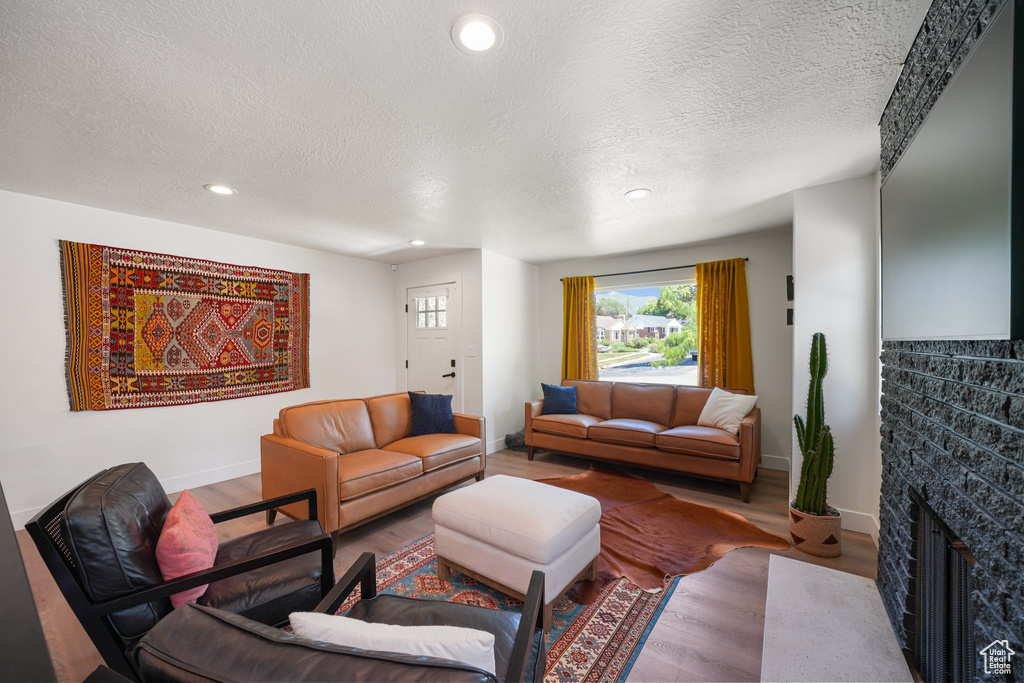 Living room with a textured ceiling, wood finished floors, recessed lighting, and a fireplace with flush hearth