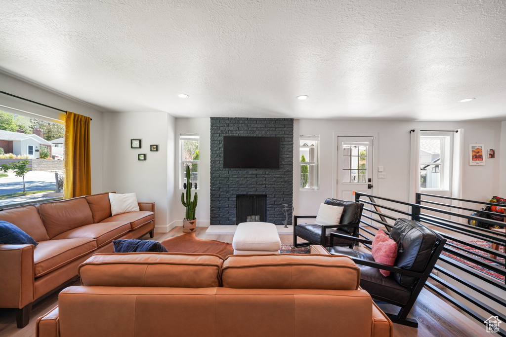 Living area featuring plenty of natural light, a brick fireplace, light wood-style flooring, a textured ceiling, and recessed lighting
