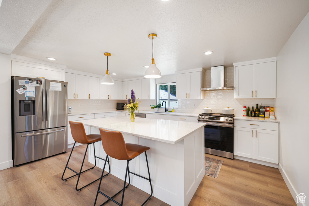 Kitchen featuring appliances with stainless steel finishes, wall chimney exhaust hood, light wood-type flooring, white cabinetry, and recessed lighting