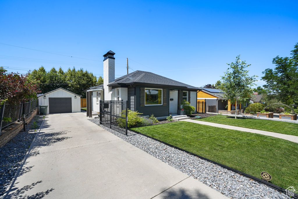View of front facade featuring driveway, a chimney, a garage, an outdoor structure, and a gate