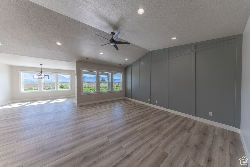 Unfurnished room with a textured ceiling, a decorative wall, ceiling fan, light wood finished floors, and a chandelier