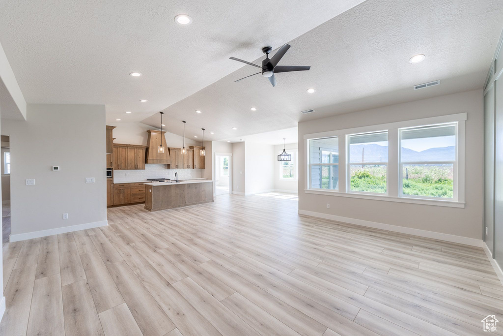 Unfurnished living room with vaulted ceiling, ceiling fan, light wood-type flooring, recessed lighting, and a textured ceiling
