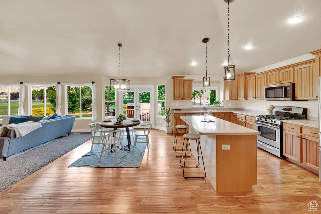Kitchen featuring appliances with stainless steel finishes, open floor plan, light countertops, a kitchen island, and a breakfast bar area