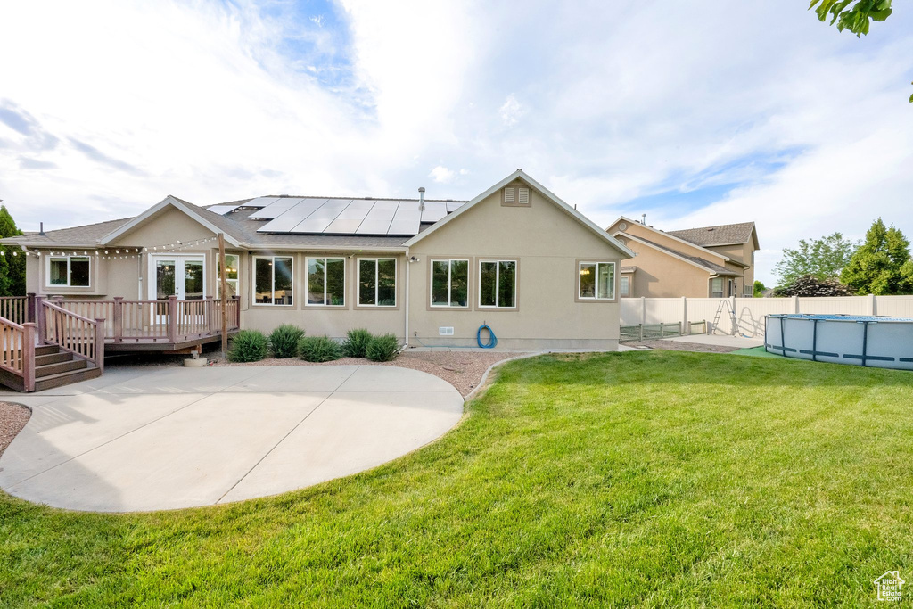 Rear view of house featuring a wooden deck, solar panels, a fenced backyard, stucco siding, and a patio area