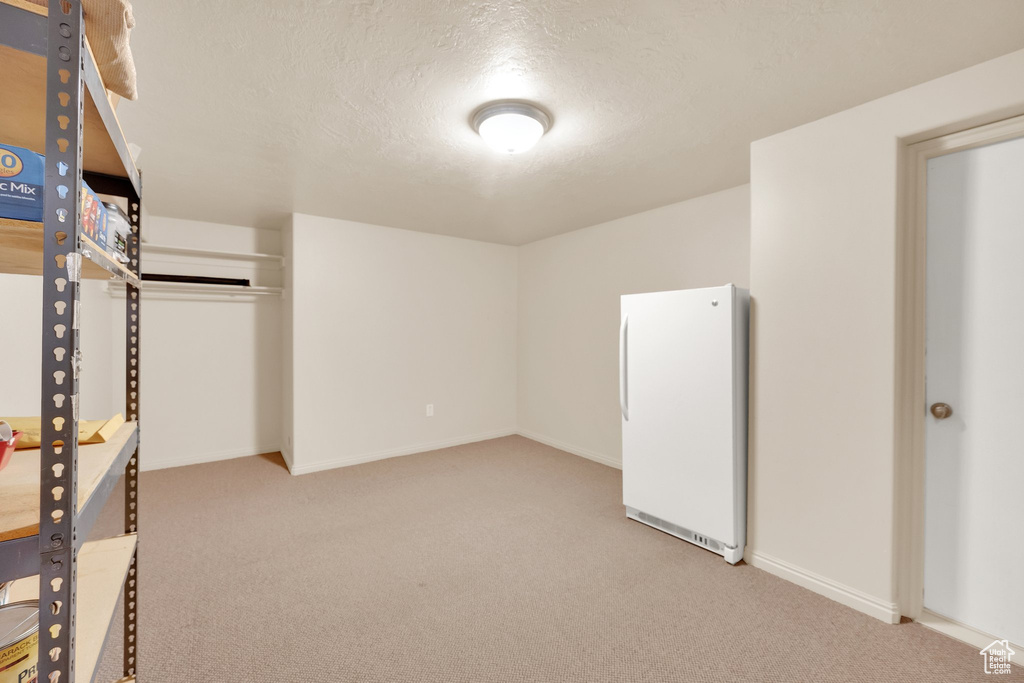Interior space featuring freestanding refrigerator, carpet floors, and a textured ceiling