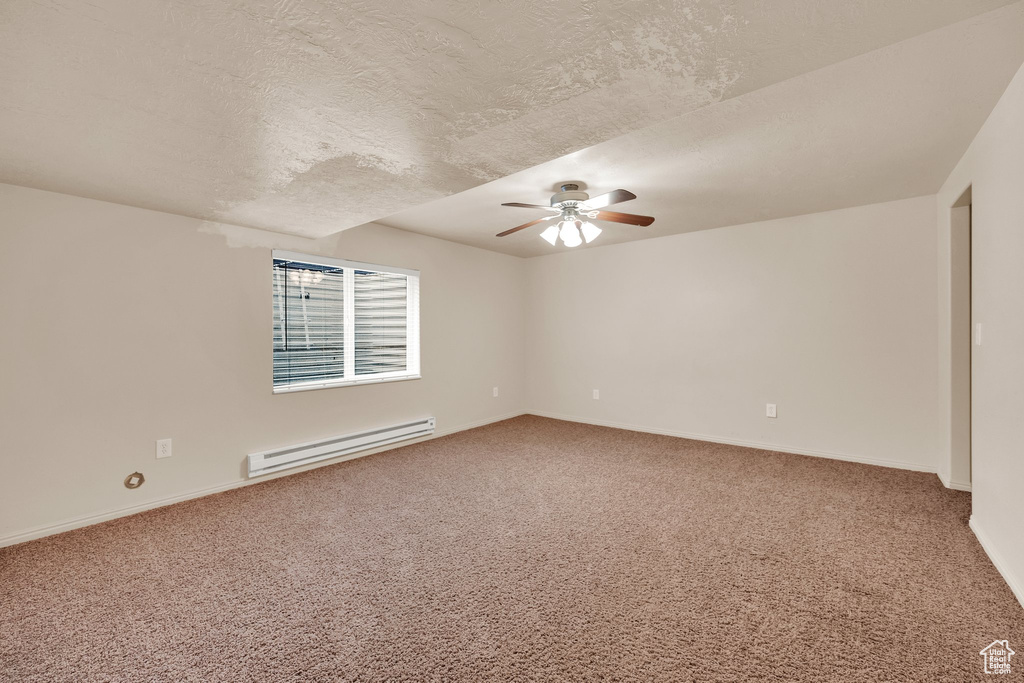 Carpeted spare room featuring a baseboard heating unit, ceiling fan, and a textured ceiling