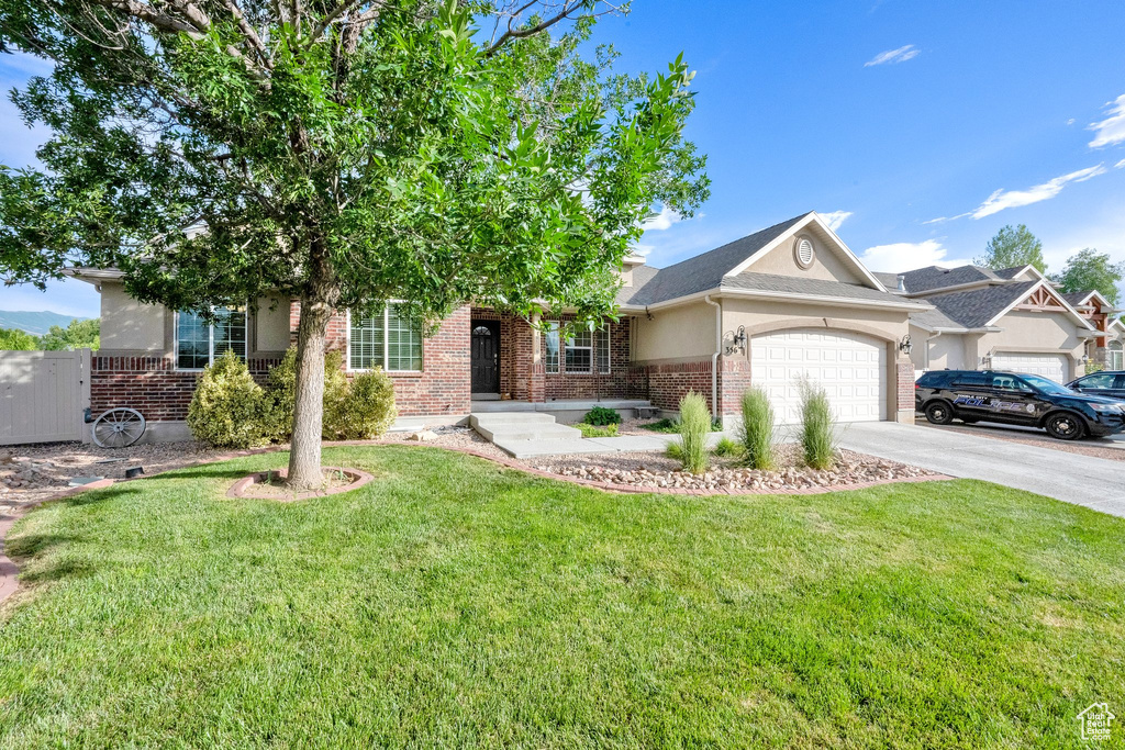 View of front of house with brick siding, a garage, a front yard, driveway, and stucco siding