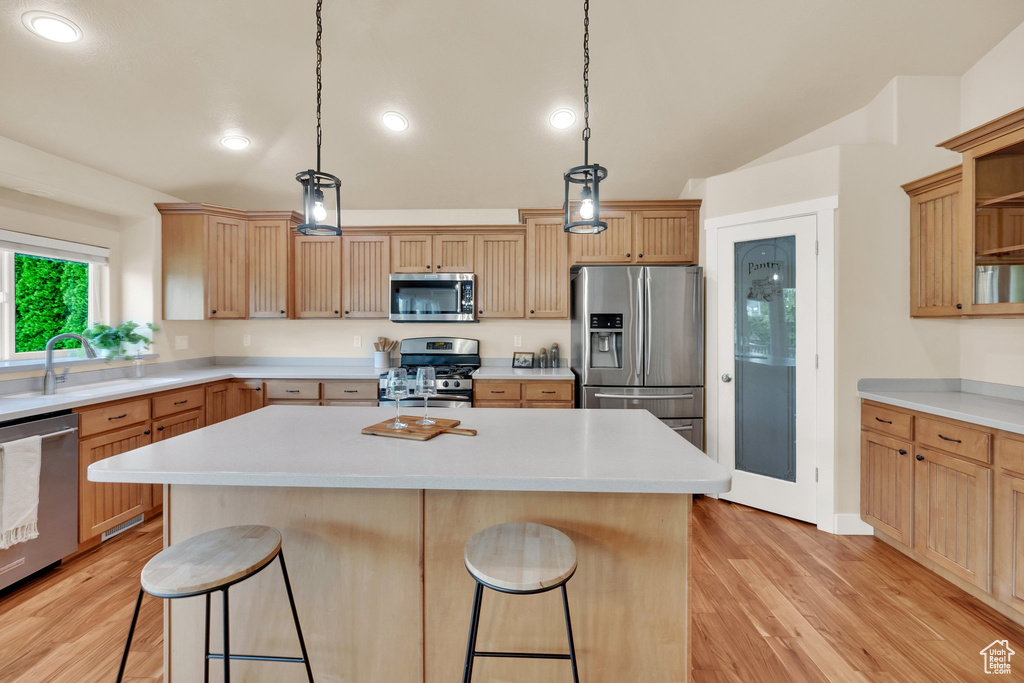 Kitchen featuring appliances with stainless steel finishes, a breakfast bar, light wood finished floors, light countertops, and vaulted ceiling