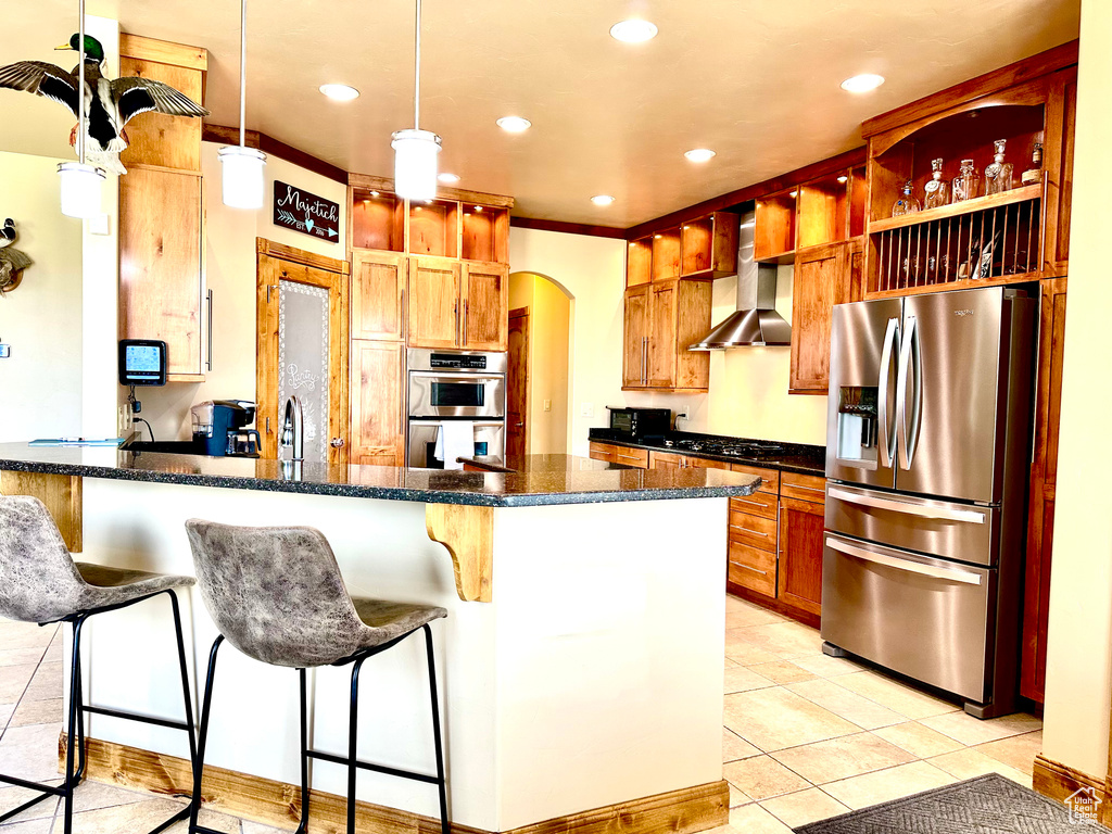 Kitchen featuring appliances with stainless steel finishes, wall chimney exhaust hood, a peninsula, light tile patterned flooring, and recessed lighting