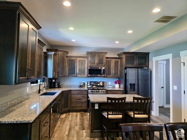 Kitchen featuring stainless steel appliances, light wood finished floors, recessed lighting, dark brown cabinets, and light stone countertops