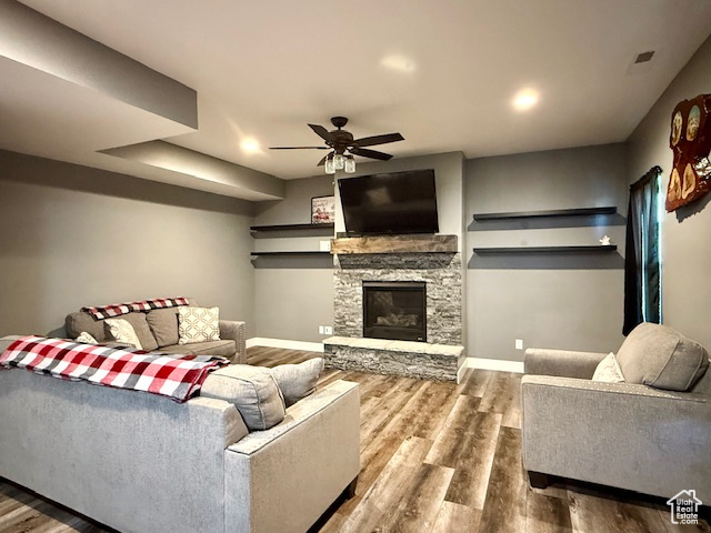 Living room featuring wood finished floors, ceiling fan, and a stone fireplace