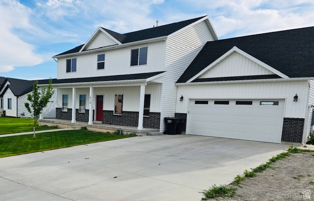 Modern farmhouse style home featuring a porch, an attached garage, driveway, brick siding, and a front yard